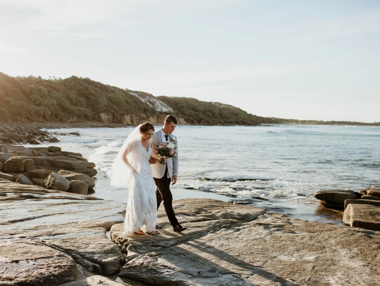 Bride and groom walking along rocky coastline