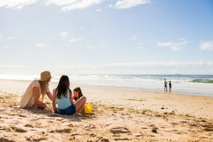 Mother with two children playing with bucket and spade in the sand