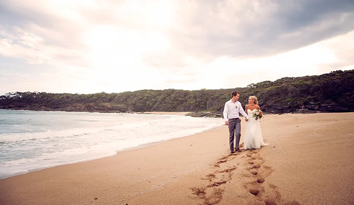 Bride and groom walking along the beach, holding hands