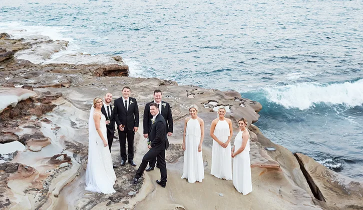 Aerial view of wedding party standing on the rocks by the ocean 
