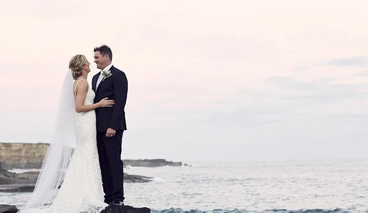 Bride and groom looking into each others eyes by the ocean