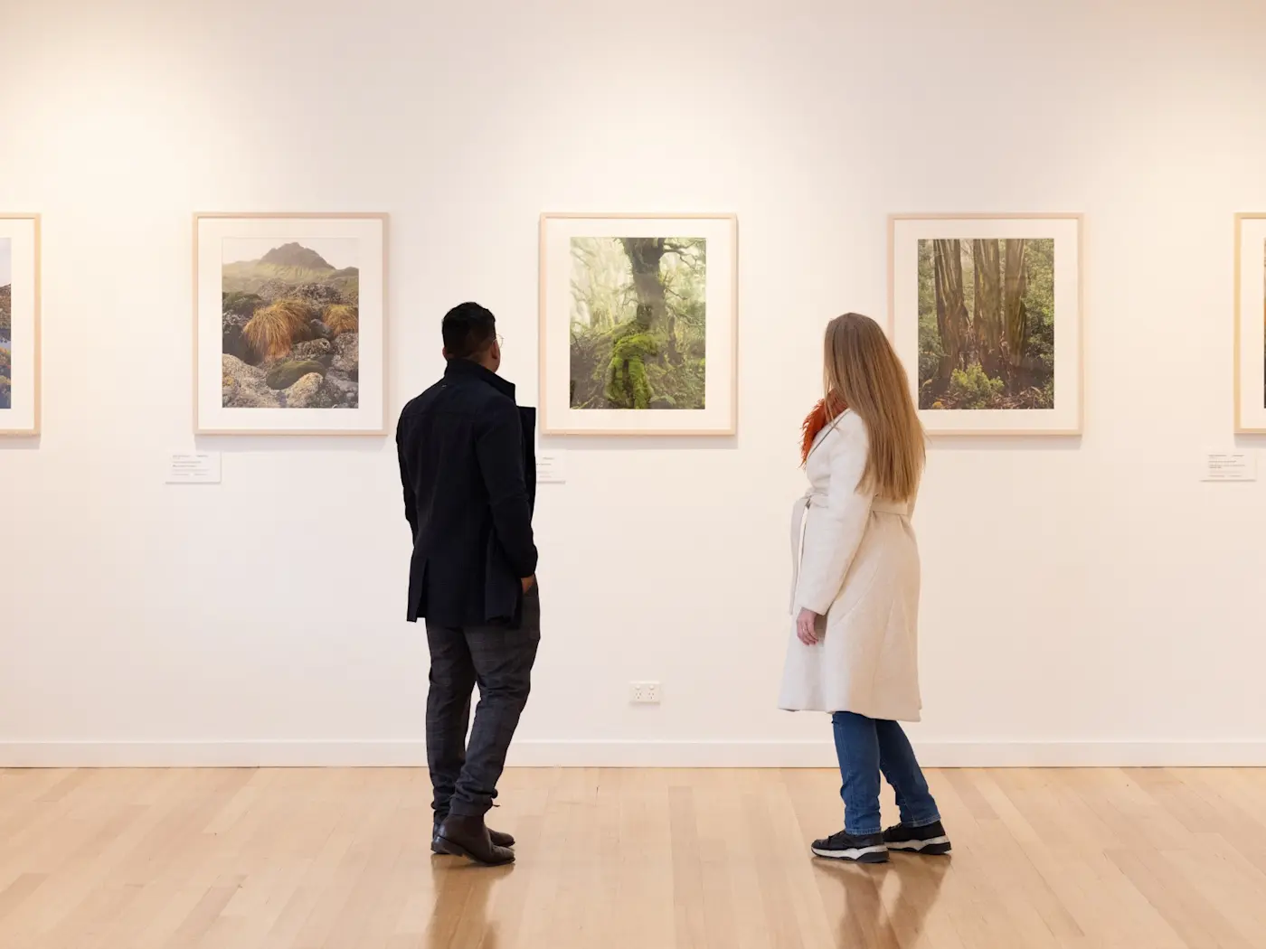 Couple viewing framed landscape art on white walls in a gallery at Cradle Mountain Hotel.