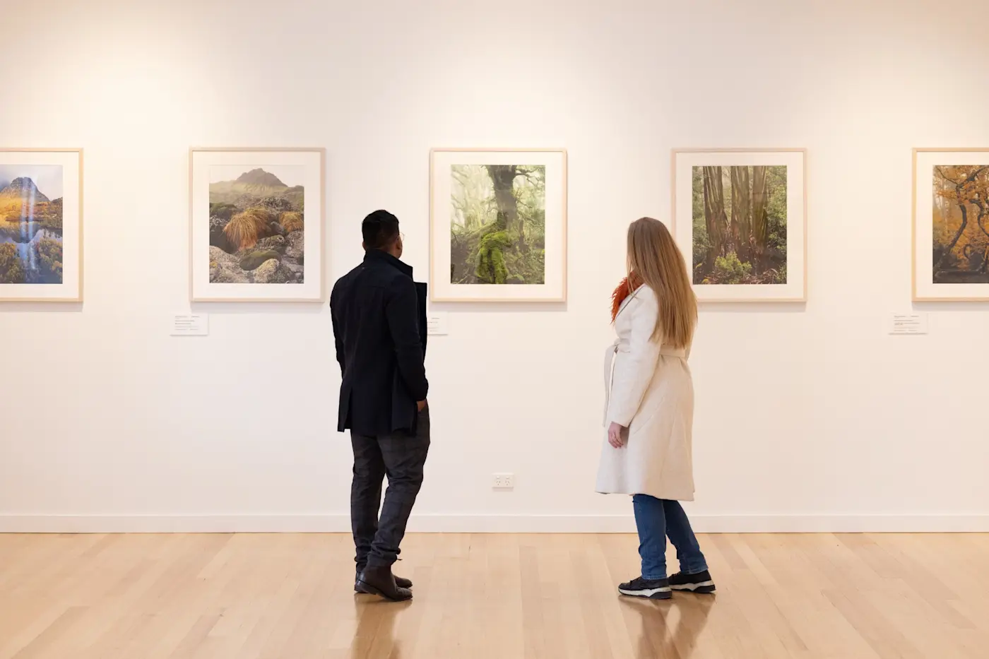 Couple viewing framed landscape art on white walls in a gallery at Cradle Mountain Hotel.