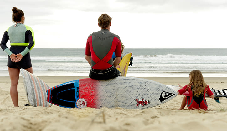 Family sitting on beach with surf boards