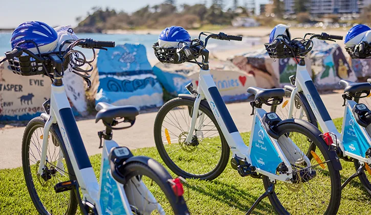 A row of e-bikes parked along a footpath near a beach