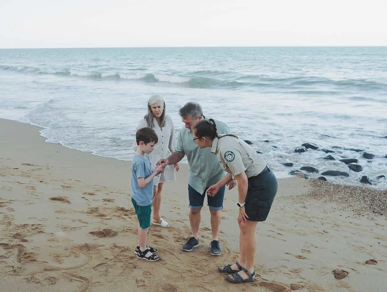 Three adults and a child inspecting something on the beach