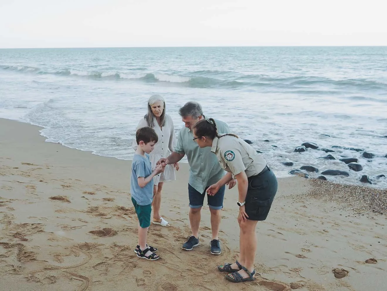 Three adults and a child inspecting something on the beach