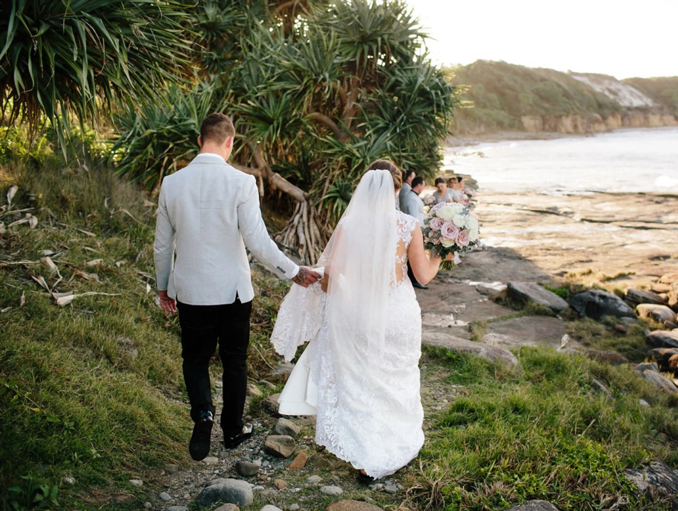 Bride and groom walking along rocky beach path