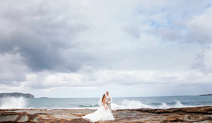 Bride and groom standing on the rocks by the ocean