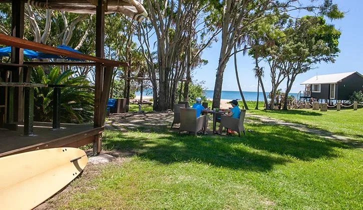 Two people stting on a table under a large tree inside an Agnes Water holiday and caravan park