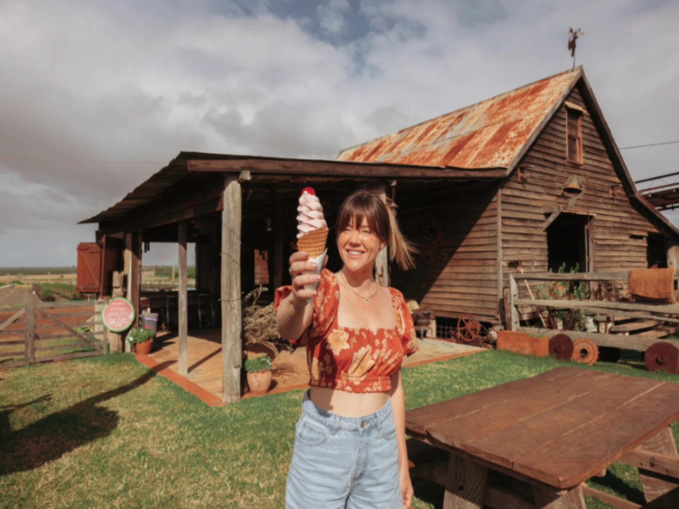 Lady in front of an old farm house, holding up an ice cream