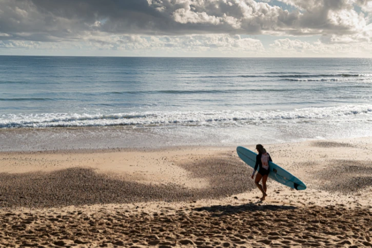 Surfer walking down the beach with a longboard