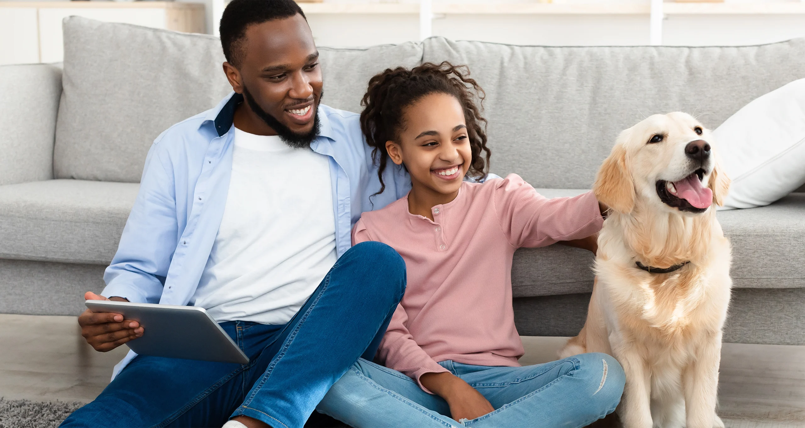 h man and daughter sitting in front of couch with ipad and yellow lab