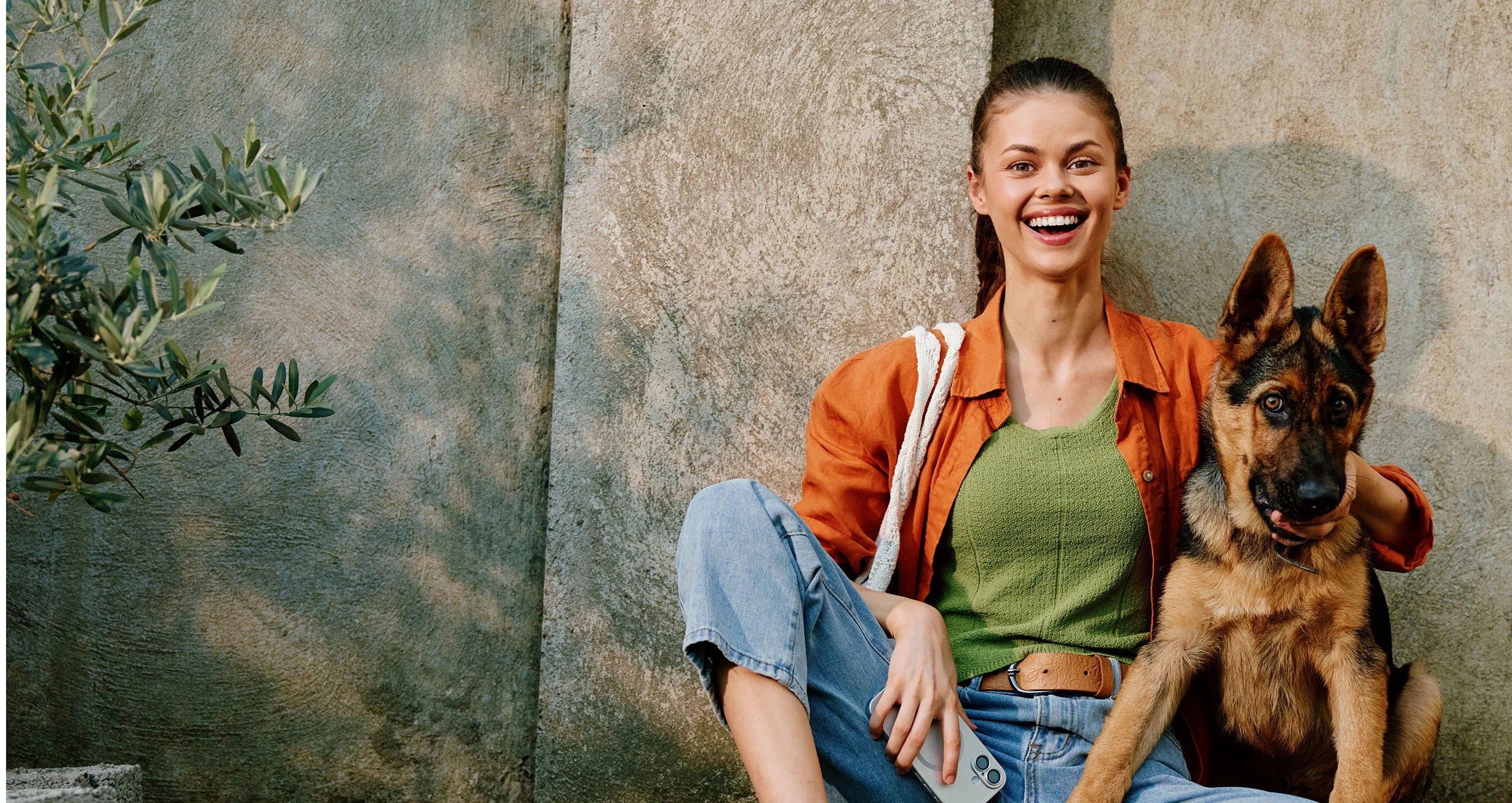h happy woman with german shepherd puppy sitting next to concrete wall