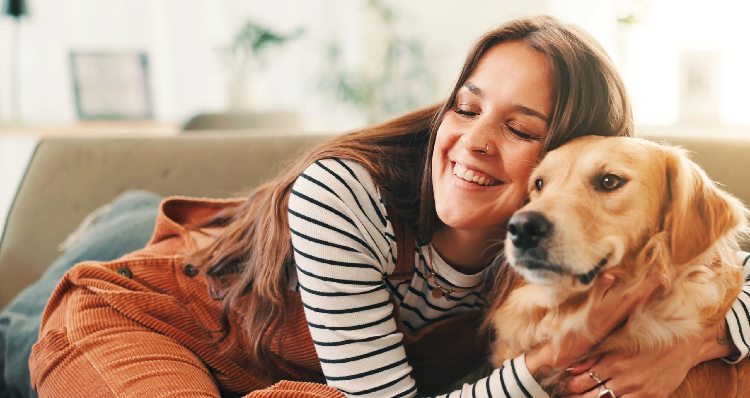 h woman in striped shirt and dark orange overalls hugging retriever
