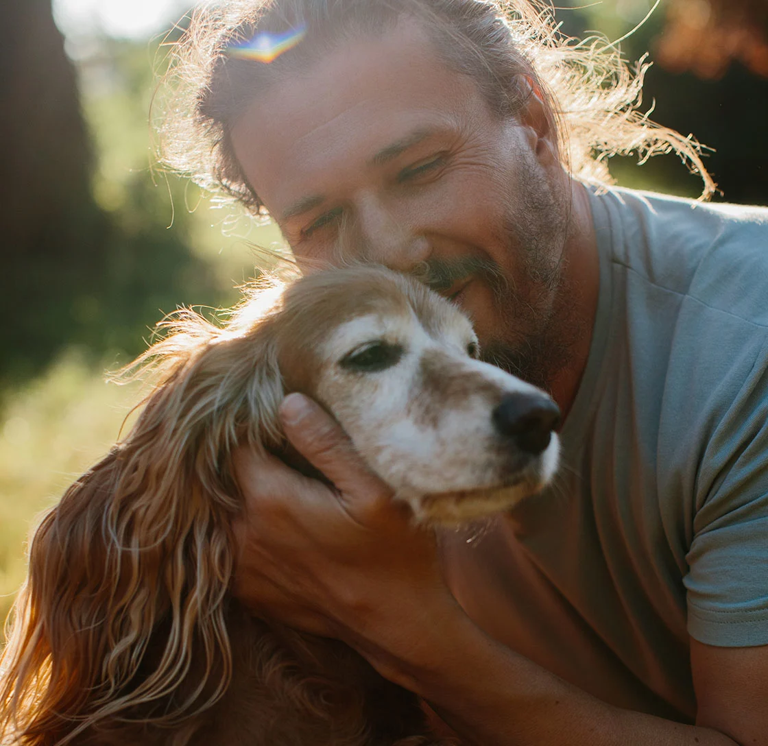 Middle-aged man cuddling his senior cocker spaniel dog in a park
