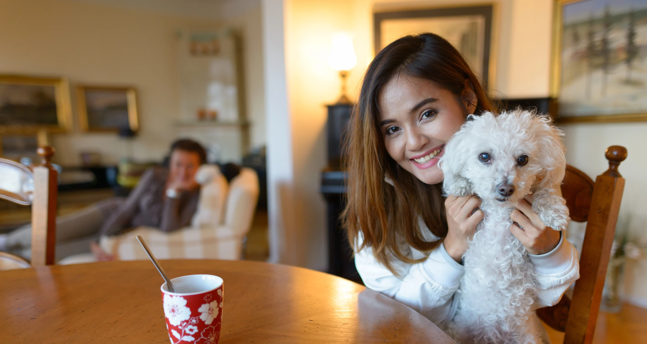 h woman holding old poodle up on kitchen table chair