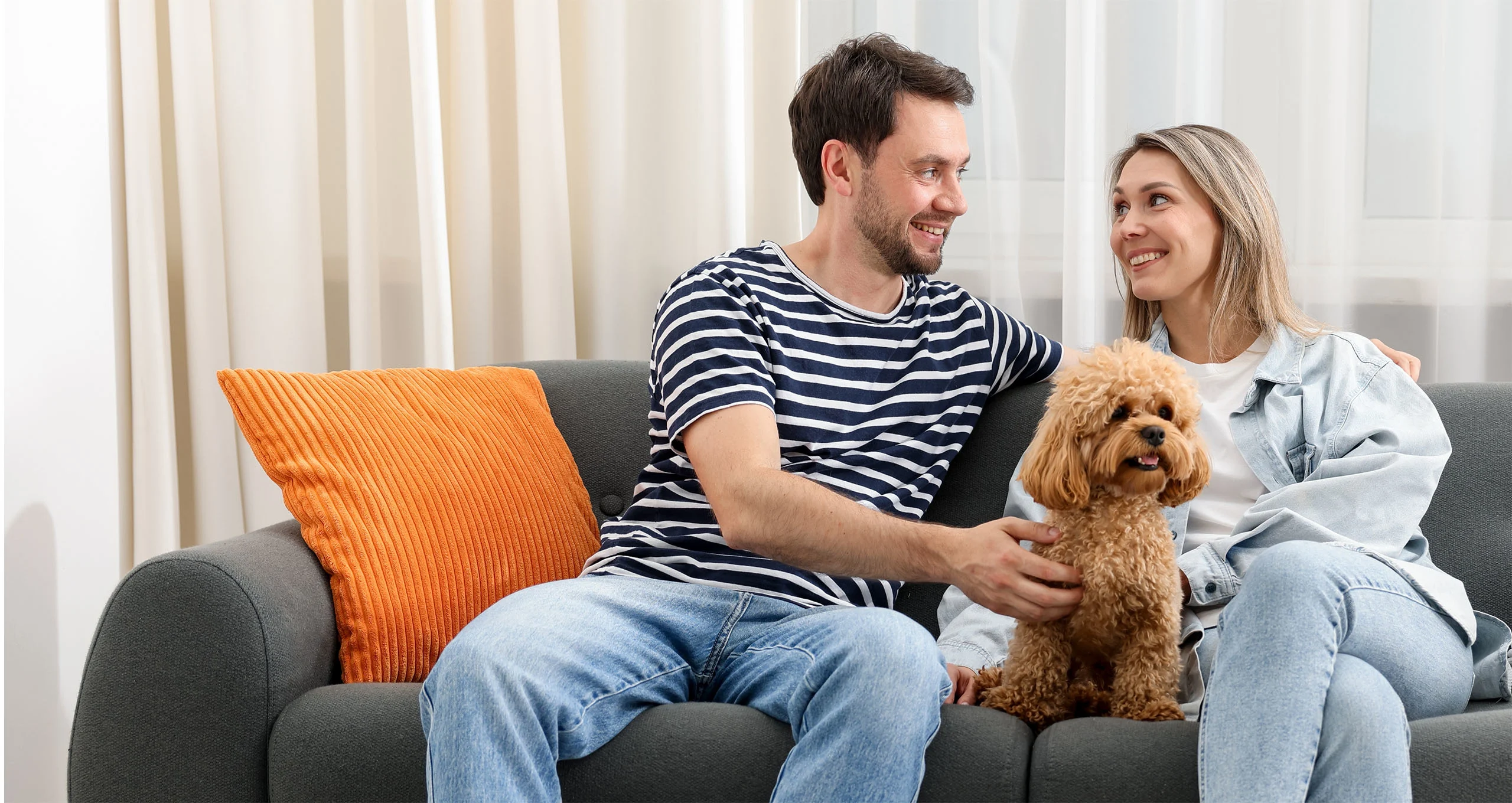 h couple sitting on couch with fluffy dark red poodle