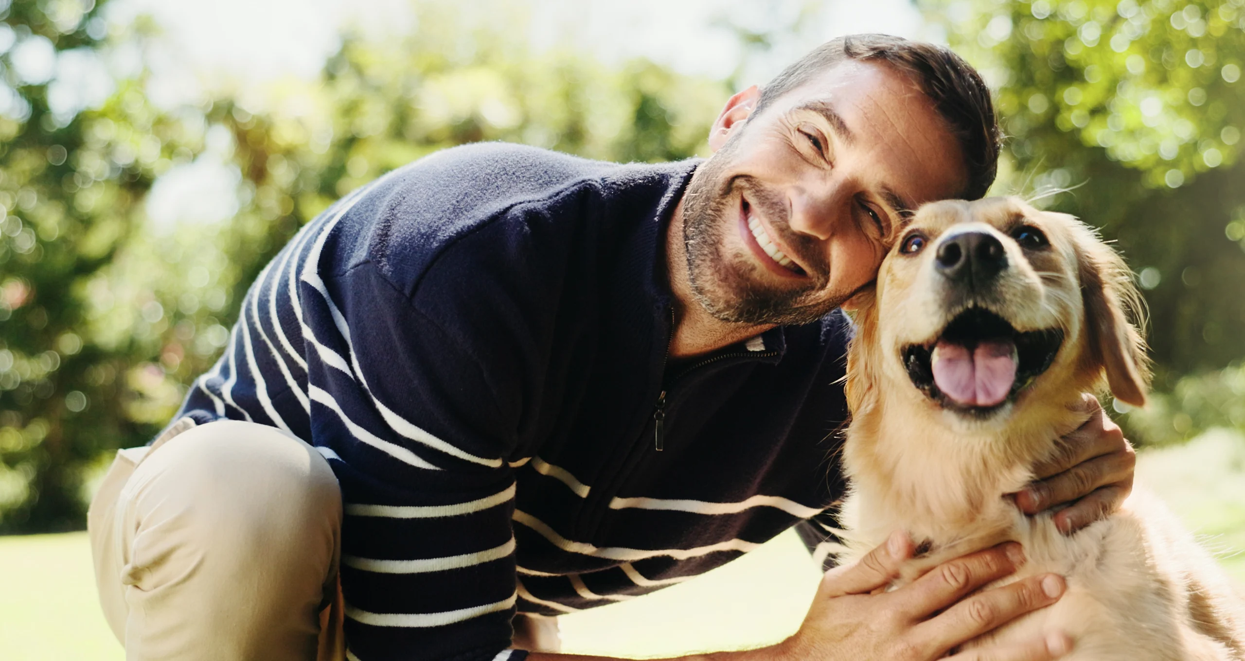 h man smiling and leaning next to golden retriever outside