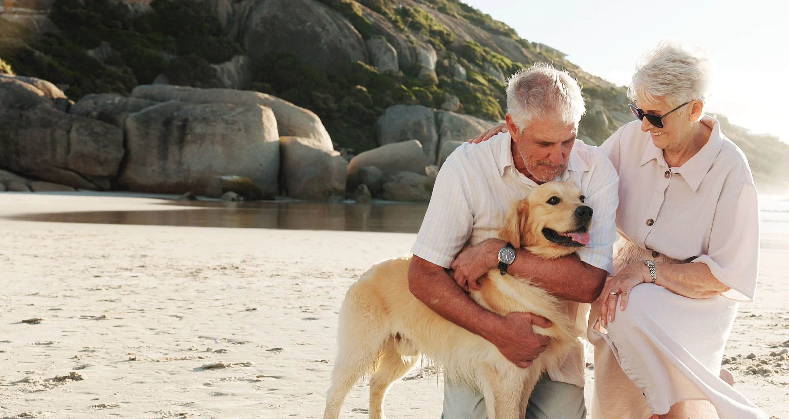 h older couple with a white golden on a beach with rocks to the left