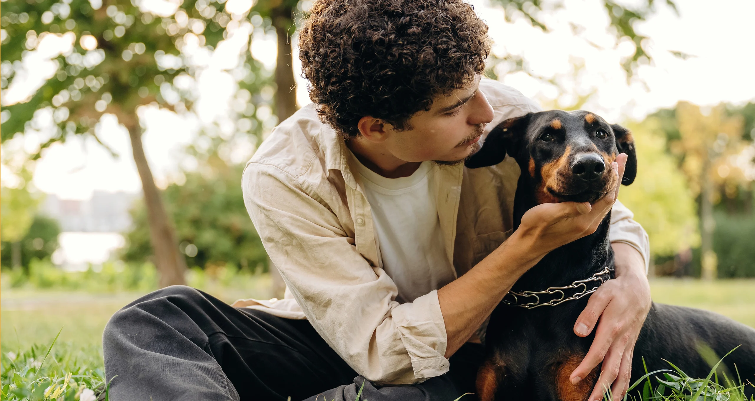 h man holding head of doberman pinscher in park