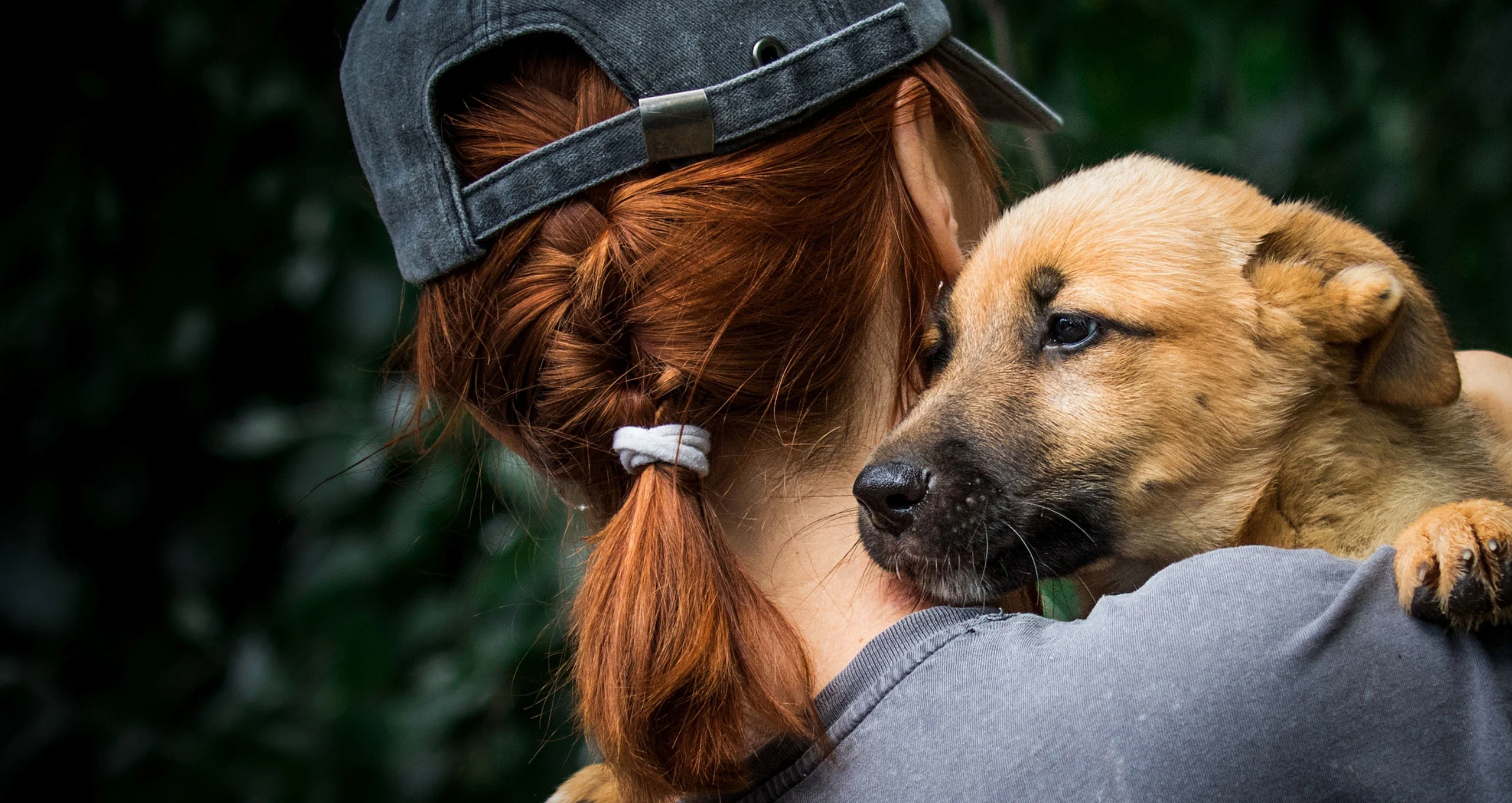 h woman with red hair in braid and in a hat with a puppy on her shoulder