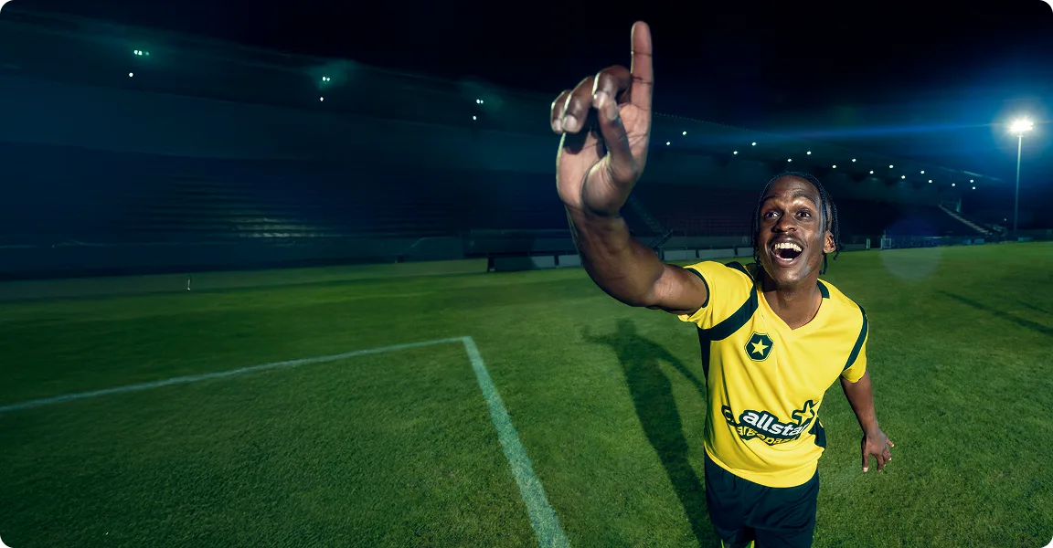 Man pointing up wearing football kit on football ground