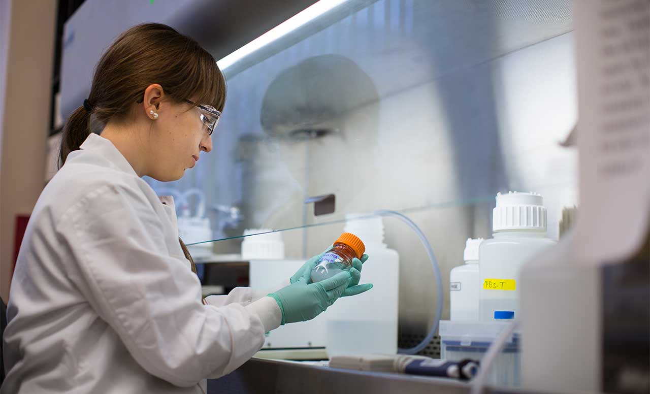 Scientist looking at a small glass jar with liquid