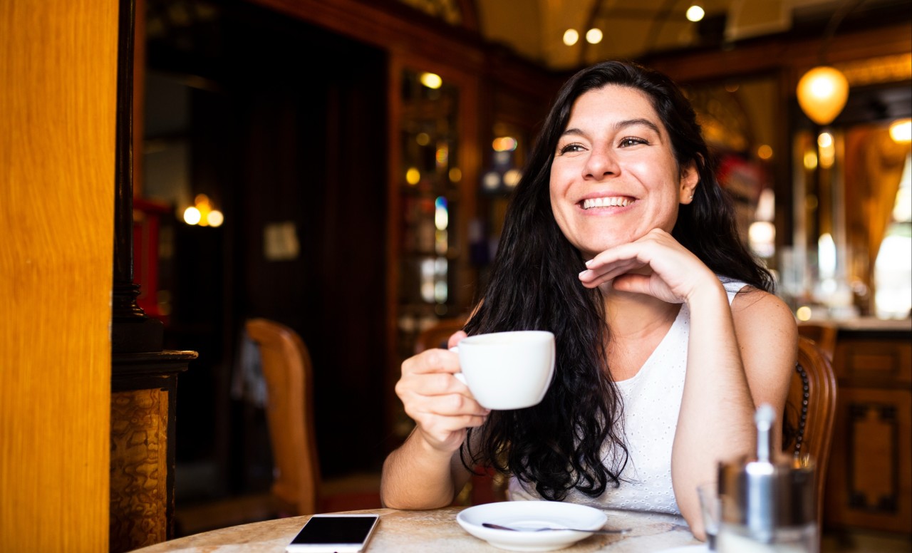 Mujer morena sonriendo tomando café
