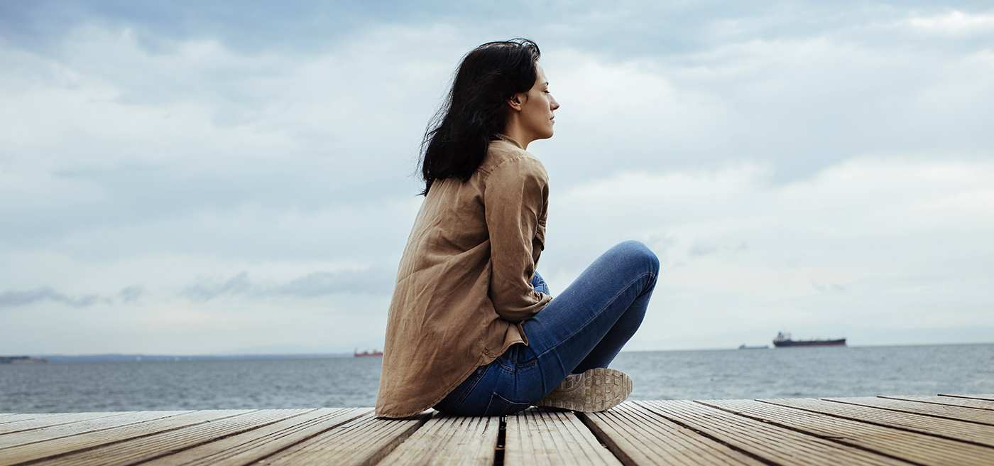 Mujer morena sentada de perfil mirando el mar
