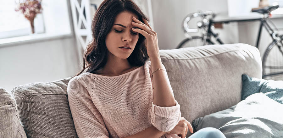 mujer sentada en un sofa sufriendo, y tocando se la cabeza