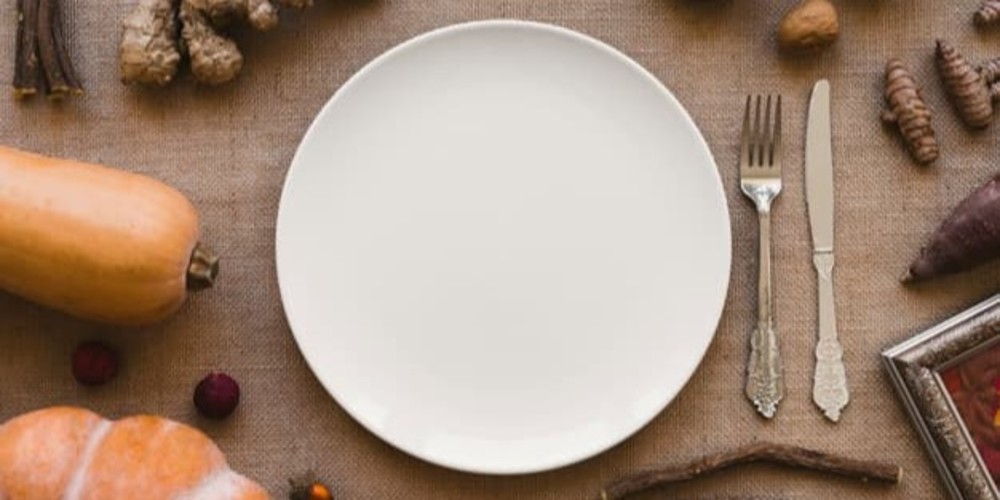 Foto de un plato blanco junto a cubiertos y alimentos
