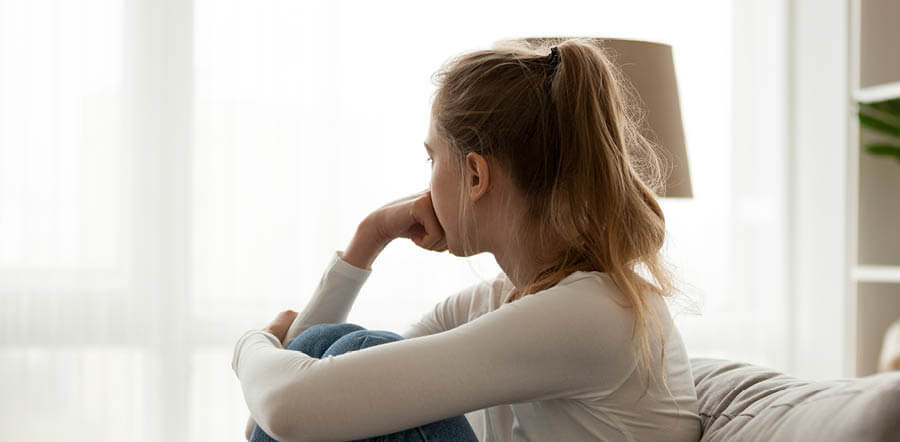 Imagen que muestra a una chica de joven edad sentada en un sofá mirando hacia la ventana 