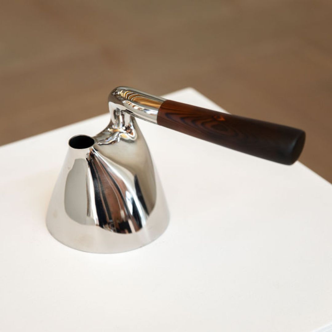 A close up of a silver kettle with a wooden handle perpendicular to the spout of the kettle