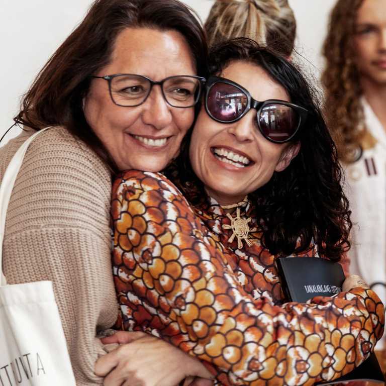 A model wearing a red ochre and orange print is hugged by an audience member