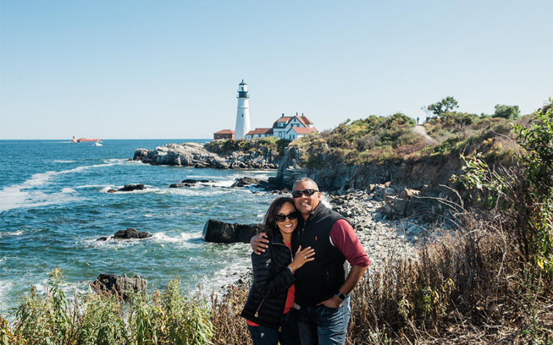 A photo of our Atlanta restaurant franchisee standing on the coast of Maine with the Portland Head Light in the background.