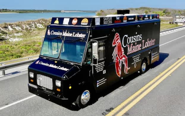 A Cousins Maine Lobster food truck that is driving down the street.