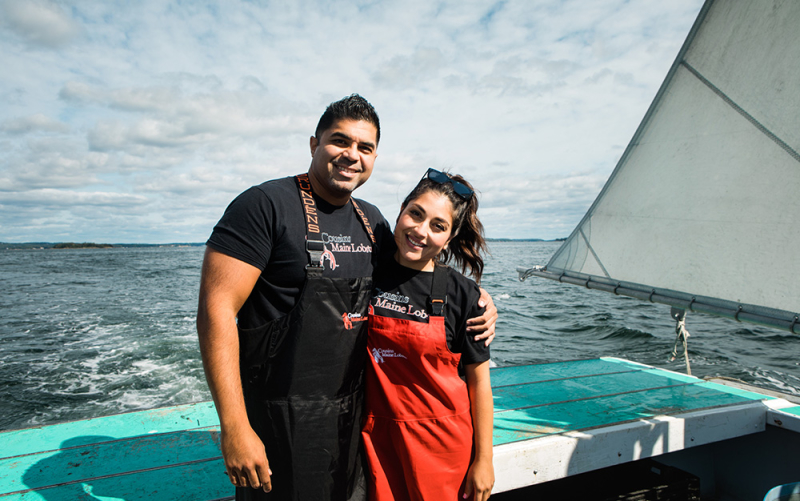 Cousins Maine Lobster franchisees stand with their arms around each other near the stern of a Lobster Boat in Maine.