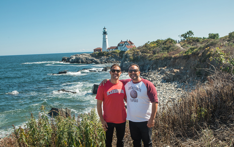 A photo of our Vegas franchisee standing with Cousin Sabin in Maine, with the Portland Head Light in the background.