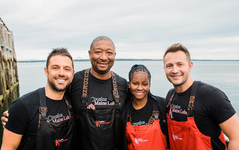 A photo of our Memphis & OKC Franchisees with Cousins Maine Lobster founders Jim & Sabin, in fishing gear in Maine