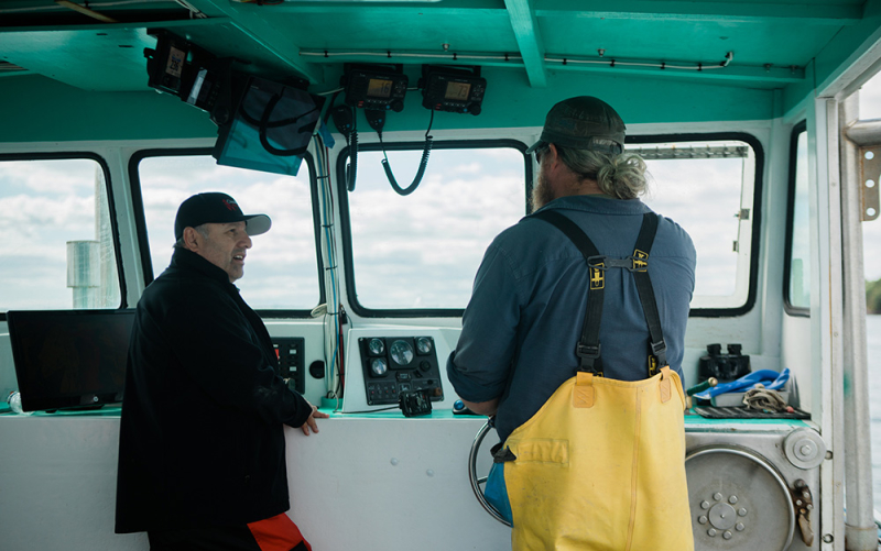 A photo of our Freehold franchisee talking with a Maine lobsterman in the cabin of his lobster boat.