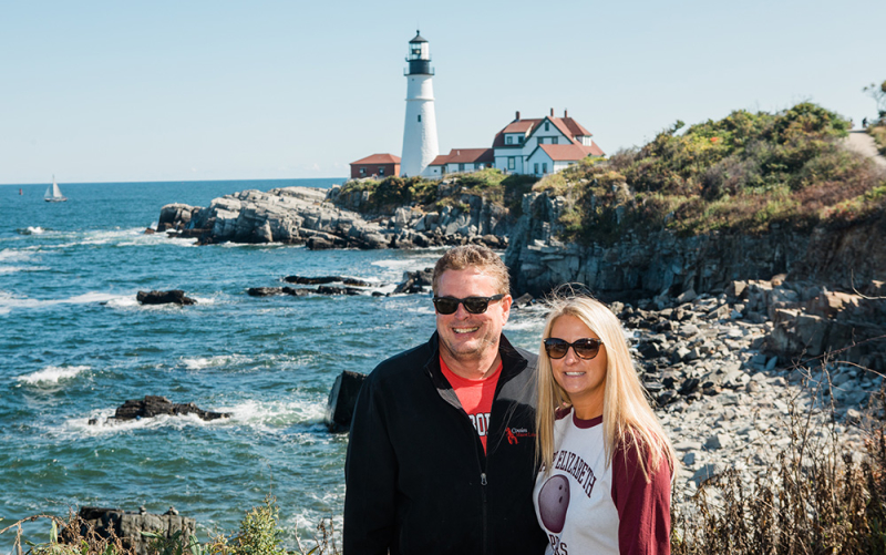 A photo of our Charlotte owners standing in Maine with the Portland Head Light behind them in the distance.