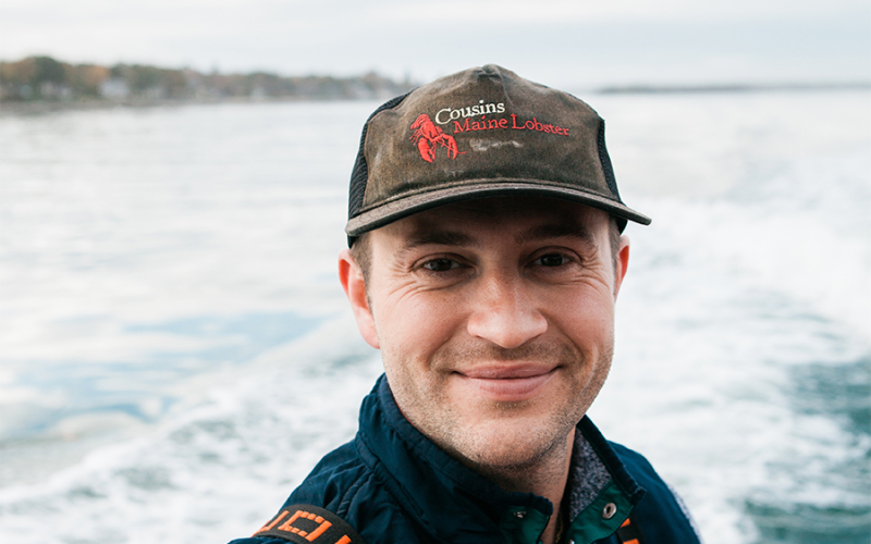 A close-up photo of Cousins Maine Lobster founder, Jim, wearing a weather Cousins Maine Lobster hat, on a fishing boat in Maine.