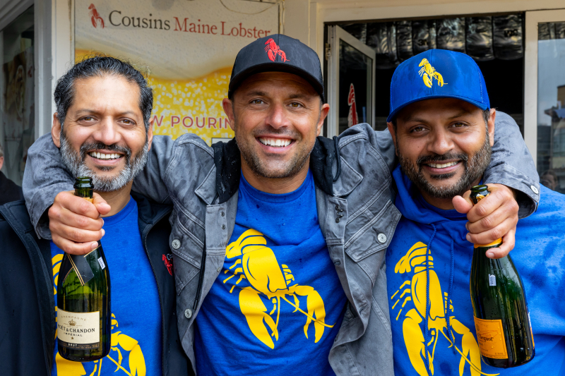 Cousins Maine Lobster Co-Founder Sabin Lomac poses for a photograph holding freshly popped bottles of Champagne with Franchisees & Brothers, Raj and Rahul Mohan