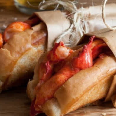 An photo of two buttery lobster rolls wrapped in brown paper and twine.