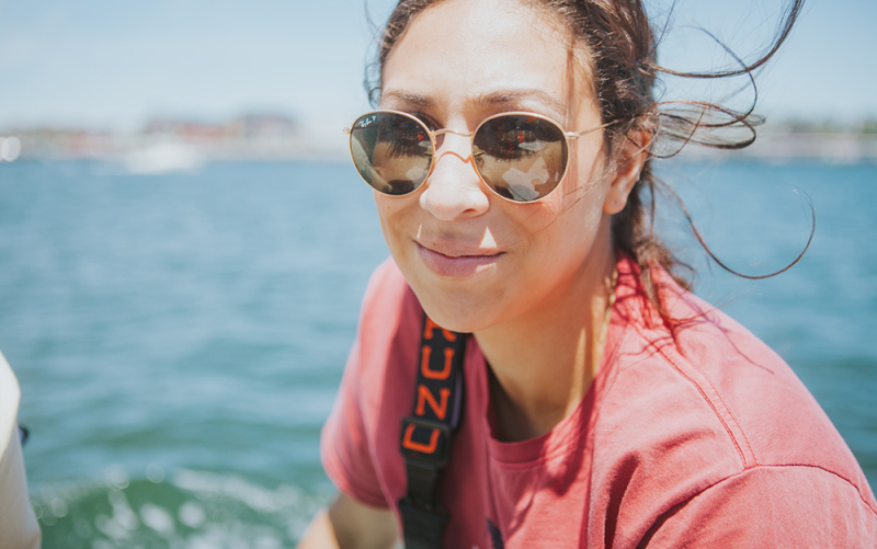 A closeup photo of our Trenton & Philly franchisee sitting on a lobster boat in sunglasses as her hair blows in the wind.