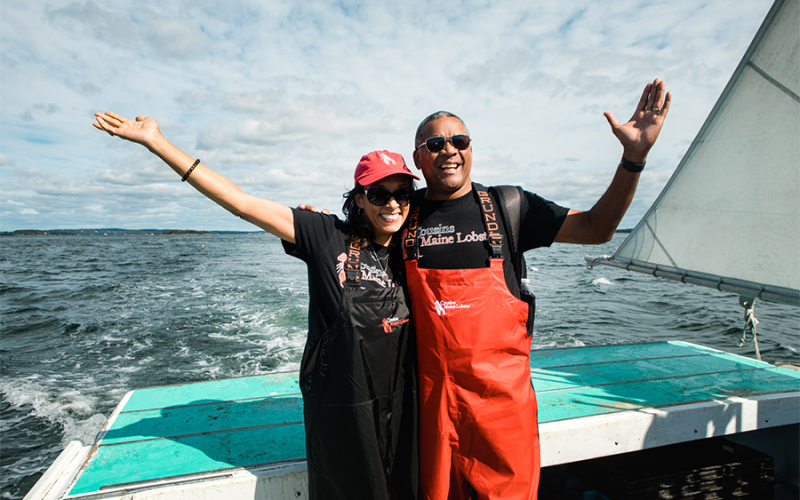 A photo of our Atlanta restaurant franchisee with his wife, both standing at the back of a lobster boat, with their arms raised in the air celebrating Maine.
