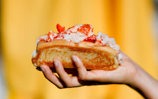 A closeup photo of a lobster roll being held in a person's hand.