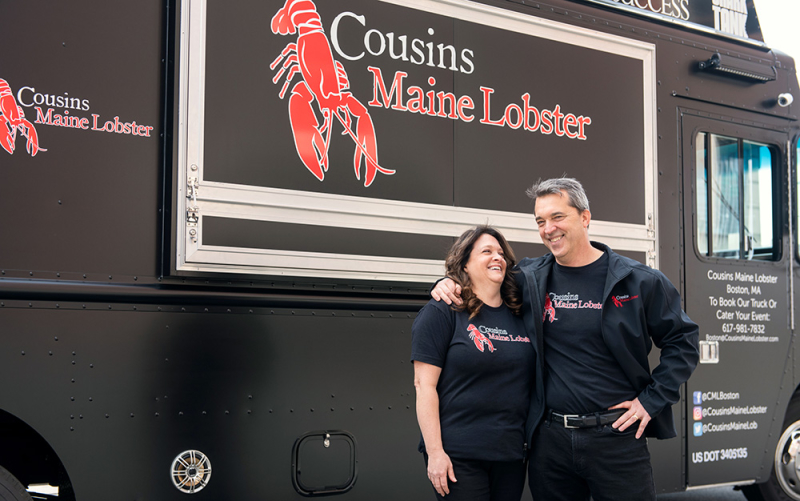 A photo of two members of our Boston family, standing with their arms around one another, in front of our Boston based food truck.