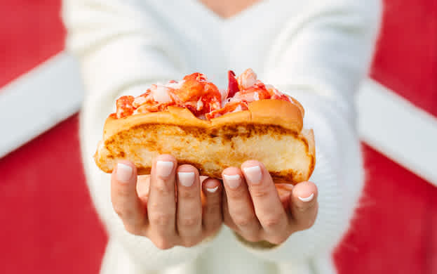 A closeup photo of a Lobster Roll held in a woman's hands.